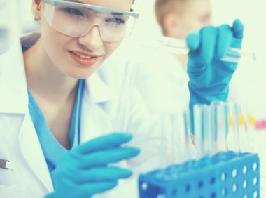 Kadın araştırmacı, beyaz arka planda izole edilmiş ilaç şişeleri ve mataralarla çevrili.