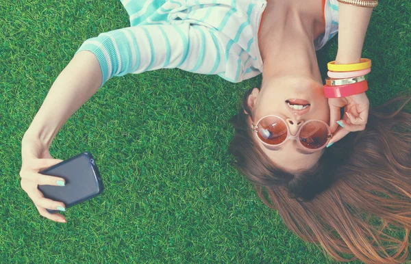 Mooie jonge vrouw selfie maken door haar telefoon liggend in groene gras — Stockfoto