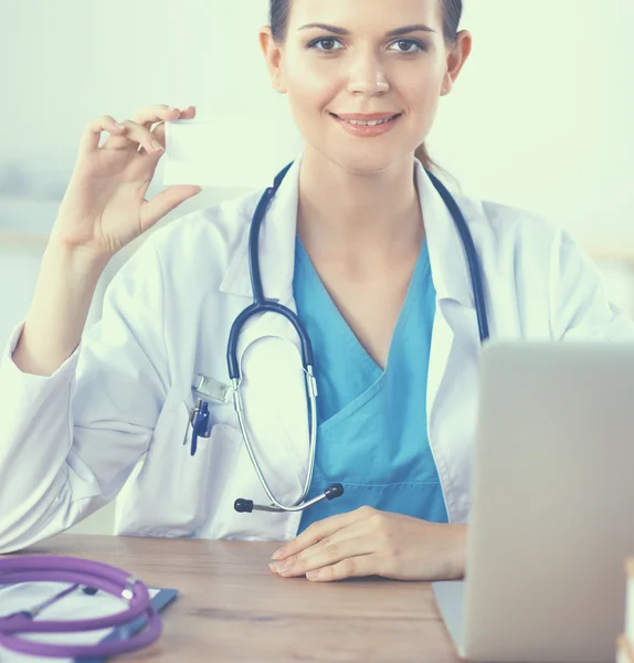 Mooie jonge glimlachende vrouwelijke arts zitten aan het bureau en schrijven. — Stockfoto