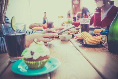 Bir grup insan ahşap masada otururken birlikte yemek yiyorlar.