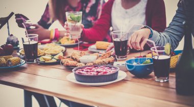 Bir grup insan ahşap masada otururken birlikte yemek yiyorlar.