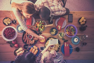 Bir grup insan ahşap masada otururken birlikte yemek yiyorlar.