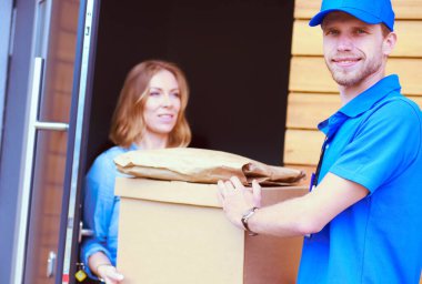 Mavi üniformalı gülümseyen kurye servis konseptine paket kutusu teslim eden teslimatçı. Mavi üniformalı gülümseyen teslimatçı.