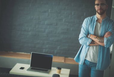 Duvarın yanında dizüstü bilgisayar tutan genç adam..