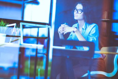 Ofis masasında dizüstü bilgisayarlı genç bir kadın oturuyor, pencereden bakıyor.