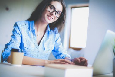 Ofis masasında dizüstü bilgisayarıyla oturan genç bir kadın.