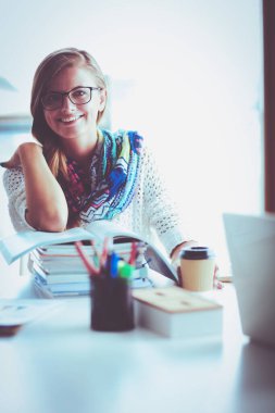 Kitapların arasında bir masada oturan genç bir kadın. Öğrenci
