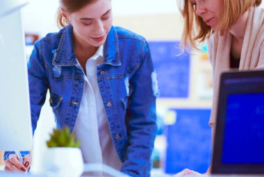 Masanın yanında duran iki genç kadın enstrüman, plan ve dizüstü bilgisayarla.