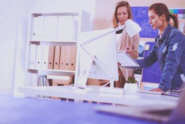 Masanın yanında duran iki genç kadın enstrüman, plan ve dizüstü bilgisayarla.