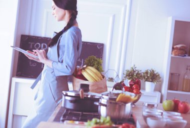 Mutfakta dijital tablet kullanan güzel genç bir kadın.