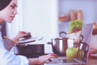 Mutfakta yemek yapmak için tablet bilgisayar kullanan genç bir kadın..