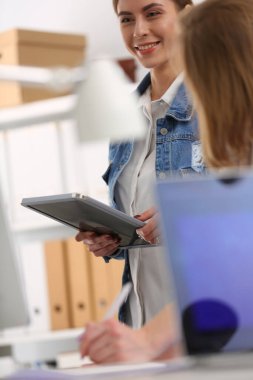 Masanın yanında duran iki genç kadın enstrüman, plan ve dizüstü bilgisayarla.