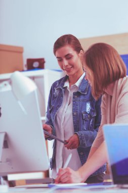 Masanın yanında duran iki genç kadın enstrüman, plan ve dizüstü bilgisayarla.