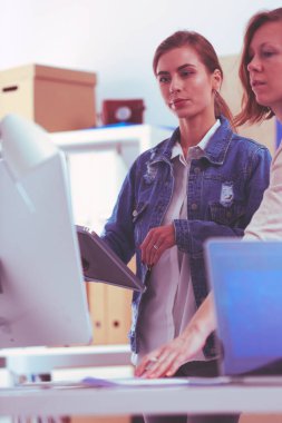 Masanın yanında duran iki genç kadın enstrüman, plan ve dizüstü bilgisayarla.