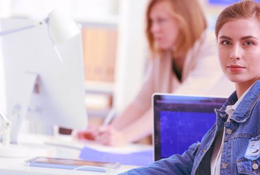 İki genç kadın masada enstrümanlar, planlar ve dizüstü bilgisayarlarla oturuyor..