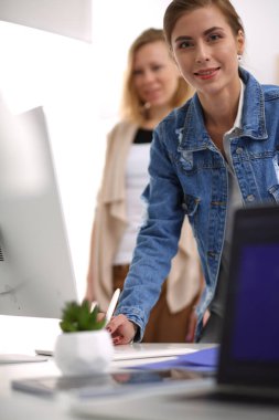 Masanın yanında duran iki genç kadın enstrüman, plan ve dizüstü bilgisayarla.