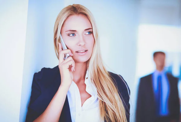 Zakenvrouw staat tegen kantoorraam te praten op mobiele telefoon — Stockfoto