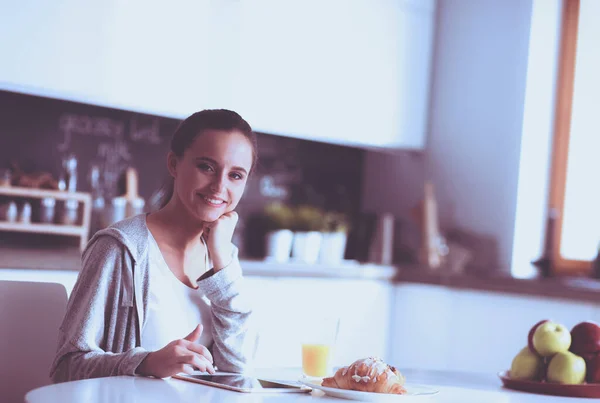 Ung kvinna med apelsinjuice och tablett i köket — Stockfoto