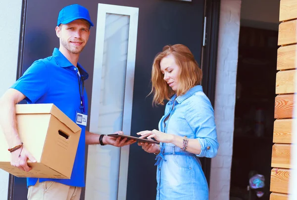 Repartidor sonriente con uniforme azul que entrega la caja de paquetes al destinatario: concepto de servicio de mensajería. Repartidor sonriente en uniforme azul — Foto de Stock