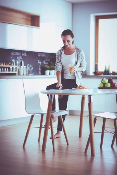 Mujer joven con jugo de naranja y tableta en la cocina. — Foto de Stock
