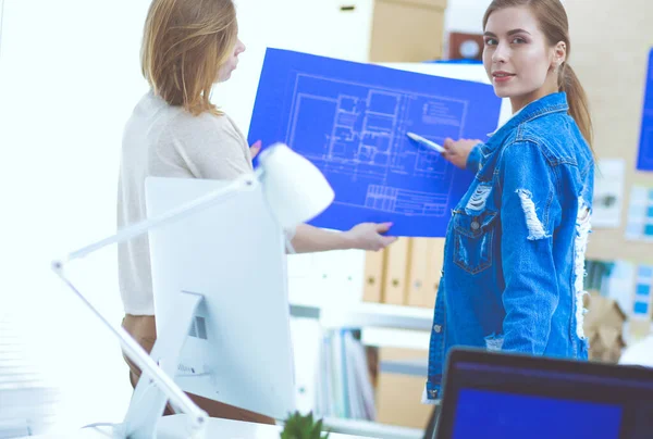 Twee jonge vrouw in de buurt van bureau met instrumenten, plan en laptop. — Stockfoto