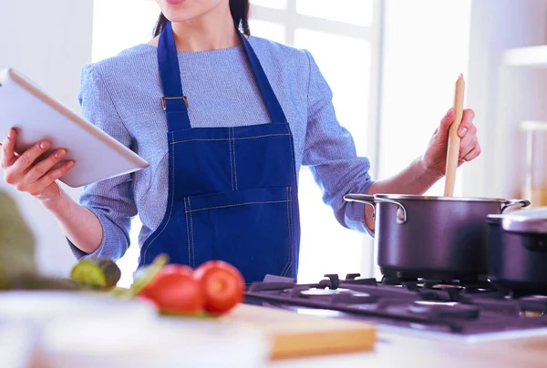 Jonge vrouw met behulp van een tablet computer om te koken in haar keuken — Stockfoto