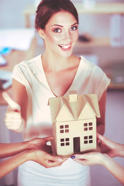 Retrato de una arquitecta sosteniendo una casita, de pie en la oficina —  Fotos de Stock