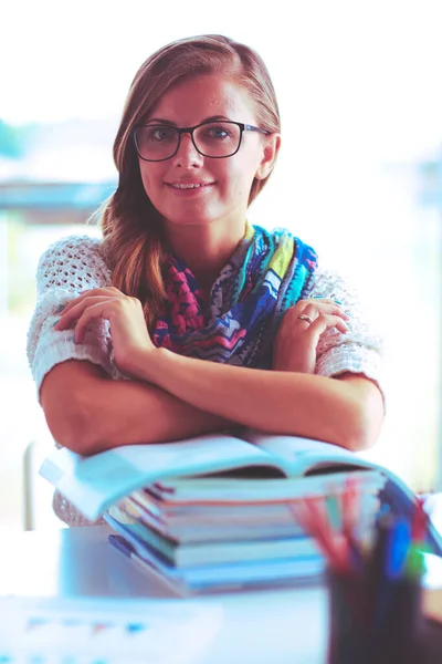 Jonge vrouw zit aan een bureau tussen de boeken — Stockfoto