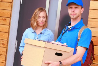 Mavi üniformalı gülümseyen kurye servis konseptine paket kutusu teslim eden teslimatçı. Mavi üniformalı gülümseyen teslimatçı.