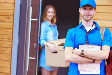 Mavi üniformalı gülümseyen kurye servis konseptine paket kutusu teslim eden teslimatçı. Mavi üniformalı gülümseyen teslimatçı.