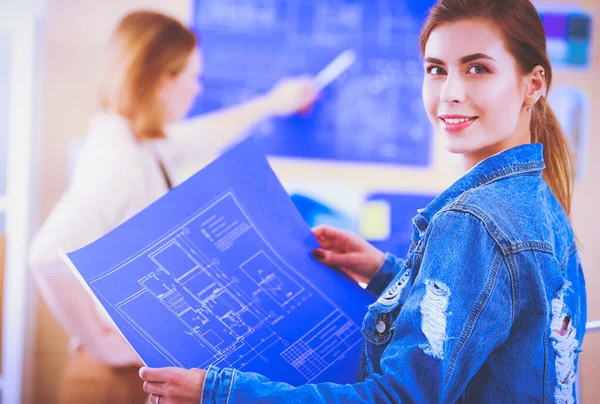 Twee jonge vrouw in de buurt van bureau met instrumenten, plan en laptop. — Stockfoto