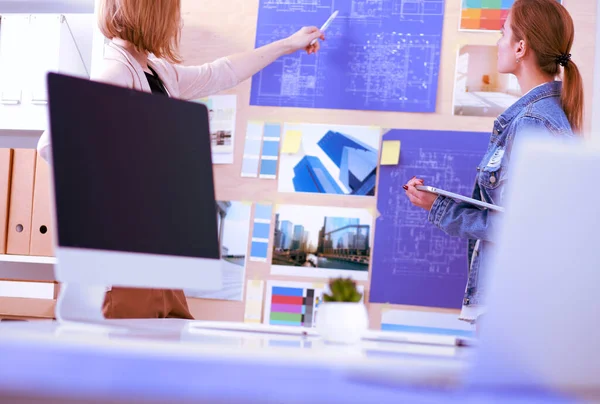 Twee jonge vrouw in de buurt van bureau met instrumenten, plan en laptop. — Stockfoto