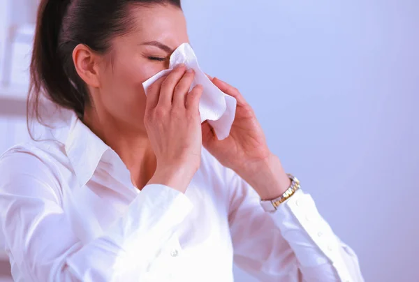 Młoda bizneswoman dmuchając nos, siedzi przy biurku — Zdjęcie stockowe