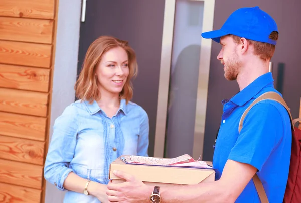 Repartidor sonriente con uniforme azul que entrega la caja de paquetes al destinatario: concepto de servicio de mensajería. Repartidor sonriente en uniforme azul — Foto de Stock