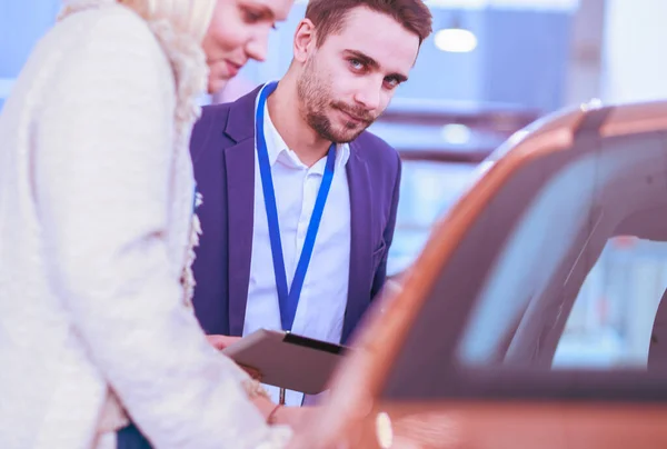 ショールームで女性とディーラーは新しい車の近くに立つ — ストック写真