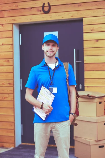 Repartidor sonriente con uniforme azul que entrega la caja de paquetes al destinatario: concepto de servicio de mensajería. Repartidor sonriente en uniforme azul —  Fotos de Stock