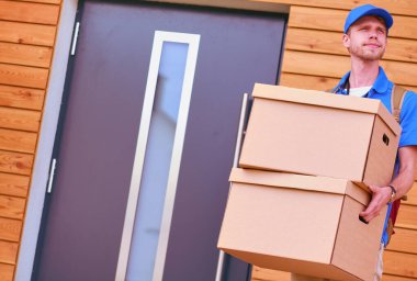 Mavi üniformalı gülümseyen kurye servis konseptine paket kutusu teslim eden teslimatçı. Mavi üniformalı gülümseyen teslimatçı.