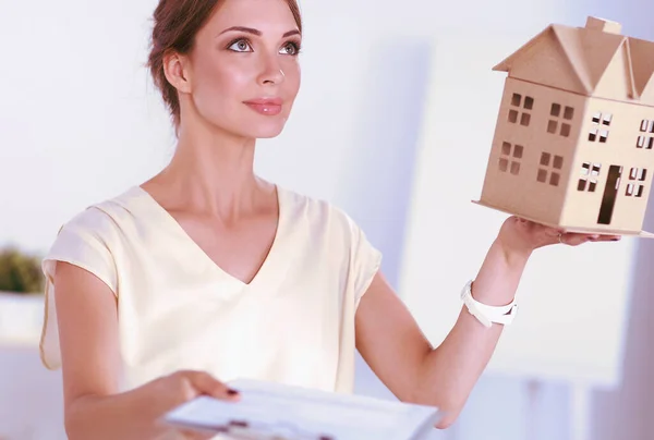 Porträtt av en kvinnlig arkitekt med ett litet hus, stående på kontoret, isolerad — Stockfoto