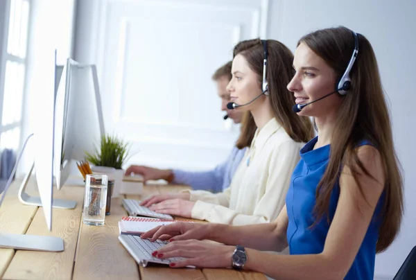 Porträt eines jungen Callcenter-Betreibers mit Headset und Kollegen, die im Hintergrund im Büro arbeiten — Stockfoto