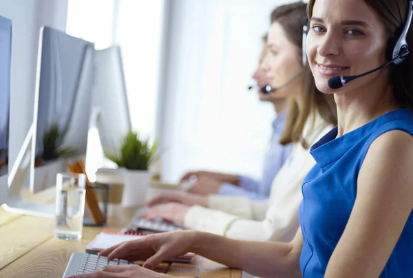 Porträt eines jungen Callcenter-Betreibers mit Headset und Kollegen, die im Hintergrund im Büro arbeiten — Stockfoto