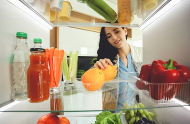 Sağlıklı yiyecek, sebze ve meyvelerle dolu açık buzdolabının yanında duran kadın portresi. Kadın portresi