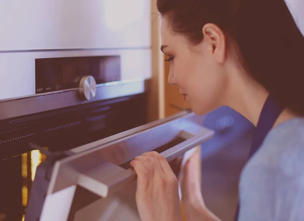 Hermosa joven comprobando cómo le va a su pastel en el horno — Foto de Stock