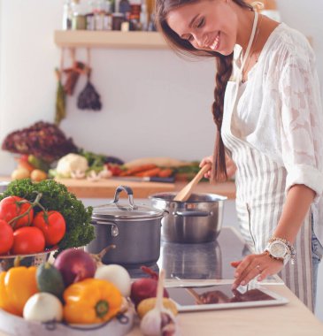 Mutfakta yemek yapmak için tablet bilgisayar kullanan genç bir kadın.