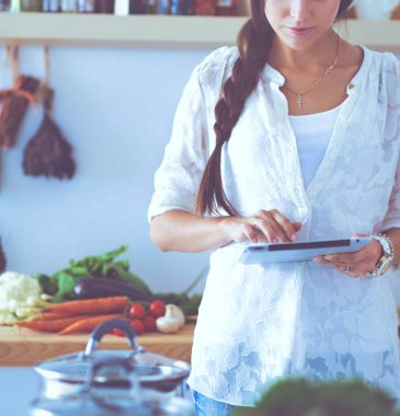 Mutfakta yemek yapmak için tablet bilgisayar kullanan genç bir kadın.