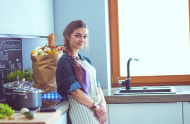 Mutfakta sobanın yanında duran genç bir kadın. .