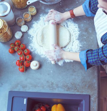 Güzel bir kadın mutfakta pasta pişiriyor. Masanın yanında duruyor..