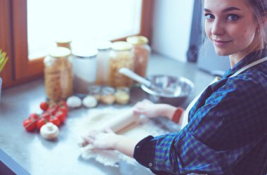 Güzel bir kadın mutfakta pasta pişiriyor. Masanın yanında duruyor..