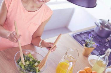 Gülümseyen genç kadın mutfakta taze salata karıştırıyor..