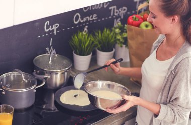 Genç bayan masanın yanında dururken mutfakta krep hazırlıyor. Mutfaktaki kadın. Mutfakta yemek yapmak..