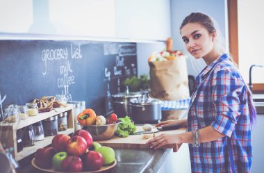 Masanın yanındaki mutfakta sebze doğrayan genç bir kadın..